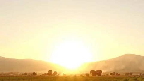 Time-lapse shot of reaping. Rice field with smoke and mountain in sunset. Stock Footage 75995350