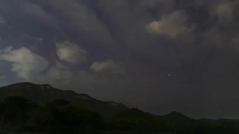 A Time Lapse of starry and mostly cloudy in night sky with a mountain. Stock Footage 230062396