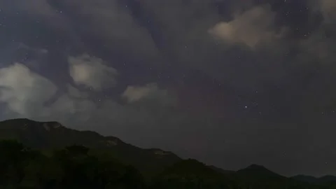 A Time Lapse of starry and mostly cloudy in night sky with a mountain. Stock Footage 232409565