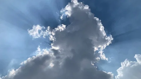 Time lapse of sun rays radiating from behind a cumulus cloud obscuring the sun Stock Footage