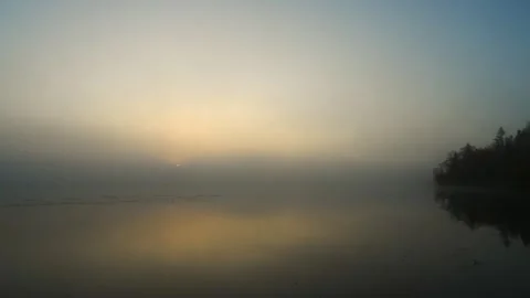Time lapse of the sun rising through a morning fog over a very calm lake  Vídeo Stock 251758088