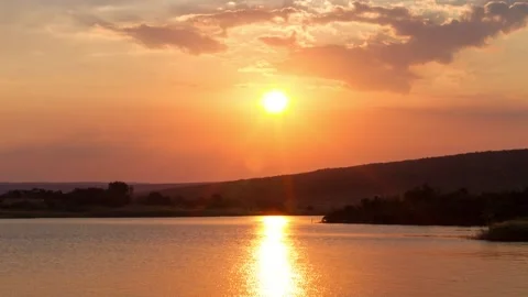 Time lapse of sun setting behind ridge across dam. Colors yellow, orange, red Stock Footage 152905552