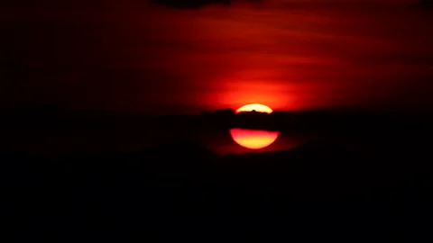 Time-lapse of the sun slowly setting behind mountain silhouettes at dusk. Stock Footage 325593851