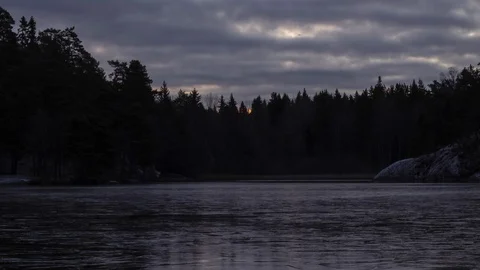 Time-lapse of sunrise and clouds moving, with light reflecting on ice of a lake Stock Footage 98888342