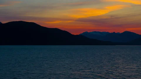 Time-lapse of a sunset behind a silhouetted mountain ridge with water in Stock Footage 52217691