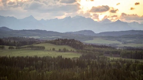 Time lapse sunset clouds above mountains with animals in a field Stock Footage