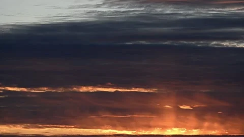 Time lapse of sunset with dark gray clouds highlighted by red orange along the h Stock Footage 288011763