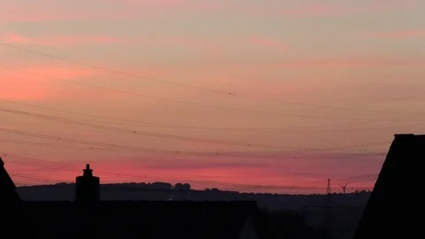 Time lapse: Sunset, sun sets behind old tiled roofs, power lines, red sky, rural Stock Footage 95434177