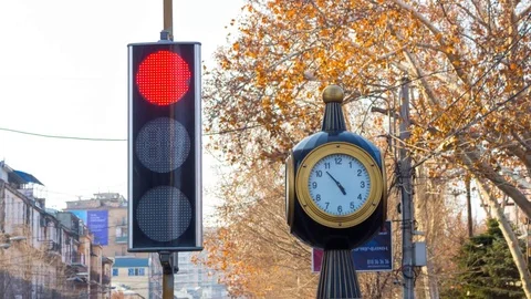 Time lapse: traffic lights with a clock on the city background with trees. Stock Footage 75350629
