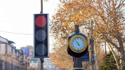 Time lapse: traffic lights with a clock on the city background with trees. Stock Footage 75350948