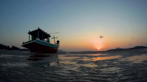 Time lapse from a tripod of the bright rising sun over a fishing boat stranded Stock Footage 155949487