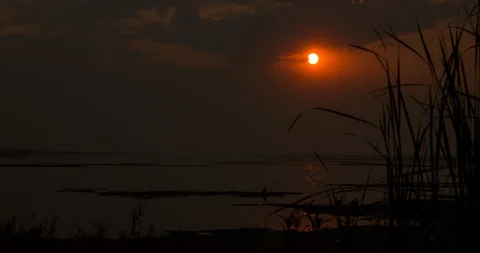 Time-lapse video at sunset, sun dips down behind the clouds over a lake. Stock Footage 95157269