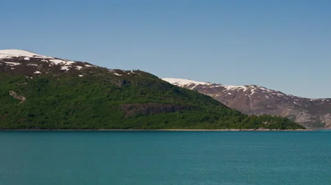 Time lapse view of green, rocky, snow capped mountains surrounded by glassy blue Stock Footage 52218013