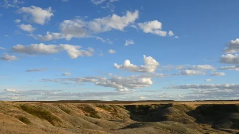 Time lapse of white clouds moving through a blue sky above a badland prairie  Stock Footage 229978242