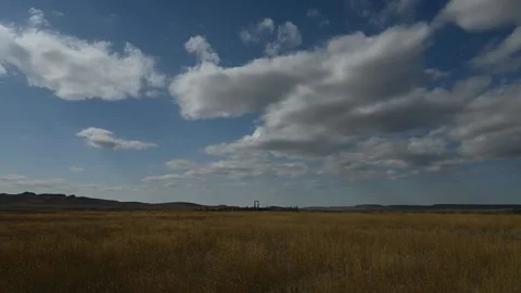 Time lapse of white clouds moving through a blue sky above a prairie landscape  Vídeo Stock 261301194