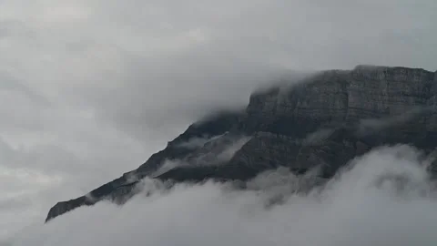 Time lapse of white misty clouds moving in front of a large rocky mountain on a  Stock Footage 300817886