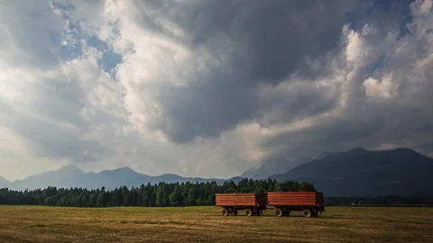 Time lapse zoom in two red tractor wagons on freshly cut harvested grass field Video stock 128969136