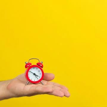 Time management concept, hand with small red alarm clock on yellow background Stock Photos
