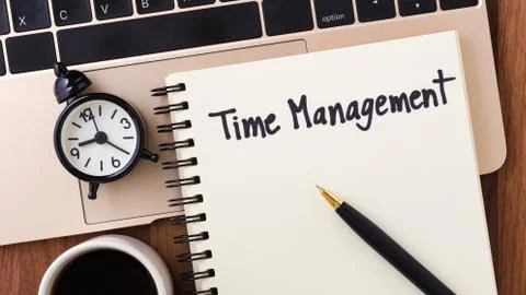 Time management concept with notebook, clock and pen on computer from top vie Stock Photos
