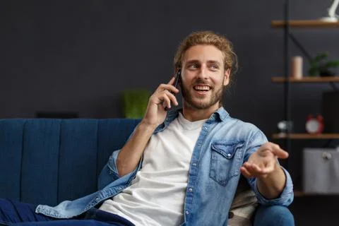 Time to relax. A curly-haired guy in a casual style, sitting on the couch at Stock Photos