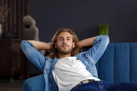 Time to relax. A curly-haired guy in a casual style, sitting on the couch at Stock Photos