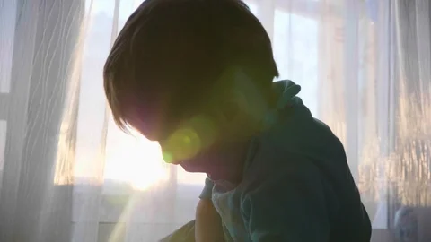The time of sunset. A small child looks at the camera near the window and smiles Video stock 87402558