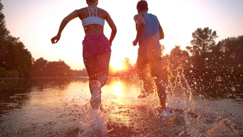 TIME WARP: Fit training partners run in refreshing river water towards sunset. 스톡 동영상 101703165