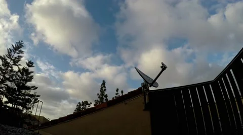 Timelapse of 2 layers of clouds during Sunset with TV dish and patio fence in Stock Footage 67522082