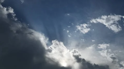 Timelapse of blue sky with white and gray clouds and sun rays rotating as the Stock Footage 336700499