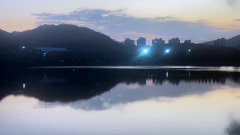 Timelapse of calm lake at dusk reflecting city skyline and mountain hills Stock Footage 337104779