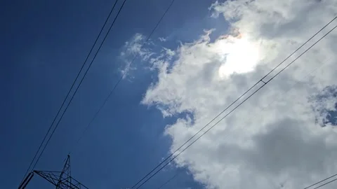 A timelapse captures white clouds moving across a blue sky. Overhead pylon wires 库存影片 337413884