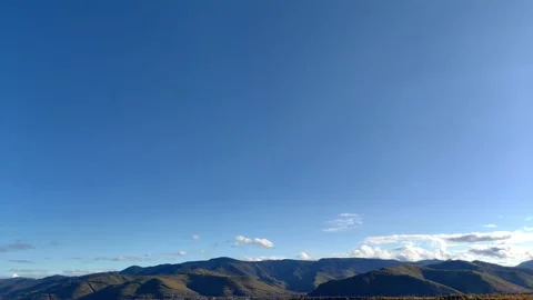 Timelapse of clear blue sky with small fluffy clouds above mountains on horizon. Video stock 302324778