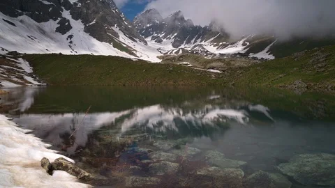 Timelapse of a clear lake surrounded by mountains. Clouds are billowing Video stock 114977874