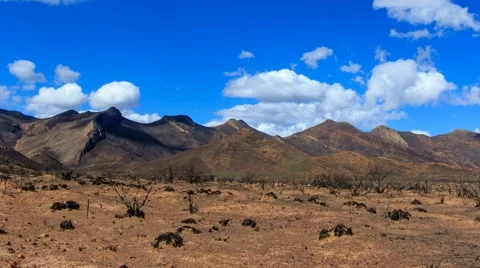 Timelapse of clouds in blue sky moving over burnt arid desert landscape Stock Footage 61943704