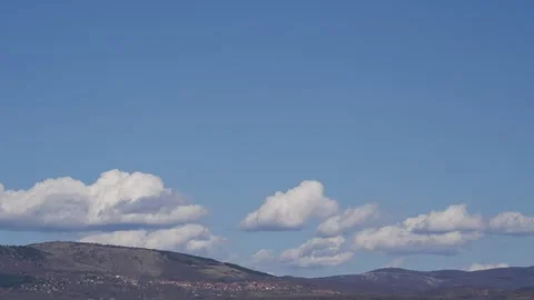 Timelapse, clouds flow over the blue sky, mountains and villages in the distance 스톡 동영상 251476731