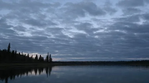 Timelapse of clouds moving above a calm northern lake at blue hour. Trees on sho Stock Footage 295077608