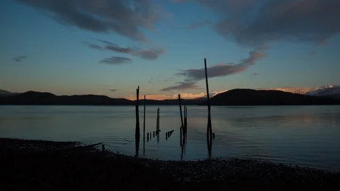 Timelapse of clouds moving across blue sky above broad lake under mountains Stock Footage 124238679