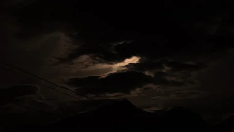 Timelapse of the clouds moving in front and covering a bright shining moon in Stock Footage 331669073