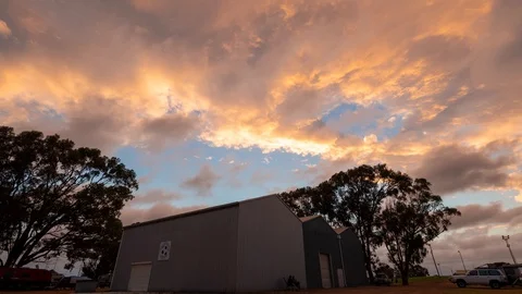 Timelapse of clouds moving in opposite directions at sunset over a tin shed Stock Footage 130109046