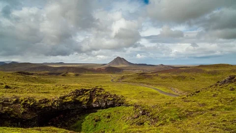 Timelapse of clouds moving over mossy field, crater and pyramid shaped mountain Stock Footage 73011279