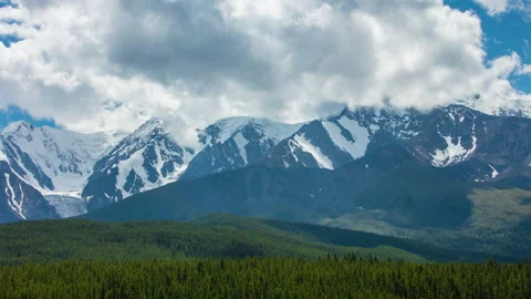 Timelapse of clouds moving quickly over snow-covered mountain peaks and taiga Stock Footage 142633457