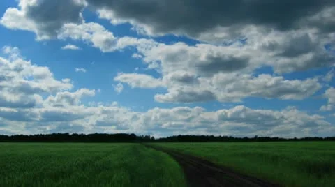 Timelapse with clouds moving to you over green field with track Stock Footage