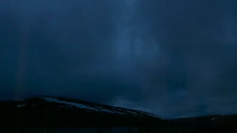 Timelapse clouds sweeping across a dark evening sky above snow-patched mountains Stock Footage 318196414