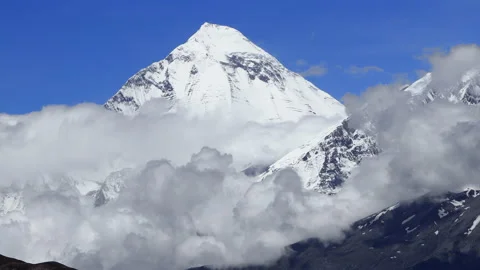 Timelapse Clouds swirl over a mountain valley, a snowy peak in the distance Video stock 155264566