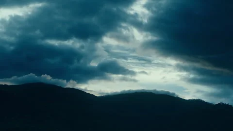 Timelapse of the dark clouds moving in the blue sky above the hills Stock Footage 261491478
