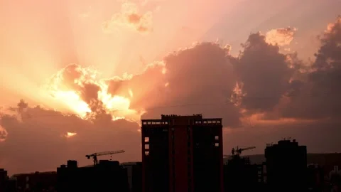 Timelapse dramatic sun rays shining through dark clouds at sunset over buildings Stock Footage 134937609
