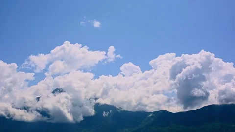 Timelapse of fluffy clouds crossing alpine summits, bathed in sunlight, during a Stock Footage 293249647