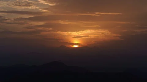 Timelapse of golden sun rising through clouds over dark mountains at dawn Stock Footage 340187401