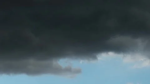 Timelapse of intense dark grey storm clouds rolling over a patch of vivid blue Stock Footage 348673854