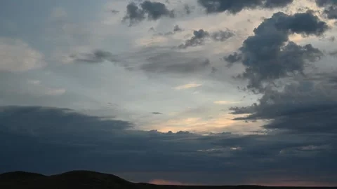 Timelapse of late day gray to yellow clouds moving above distant rolling Stock Footage 310690679